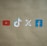 Four social media platform logos are arranged on a brown background. From left to right, the logos are for YouTube in red, TikTok in a combination of red, blue, and white, X in white, and Facebook in blue.